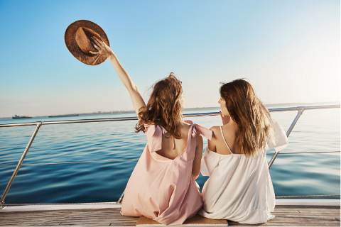 back-portrait-of-two-female-friends-sitting-on-boat-waving-with-hat-while-talking-and-enjoying-looking-at-seaside-sisters-finally-took-vacation-to-vis